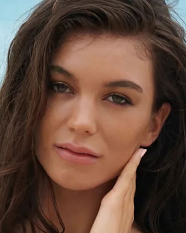 Erin Willerton poses in front of the ocean and looks at the camera.